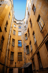 Fototapeta premium Saint Petersburg, Russia, 17 October 2021: Hight narrow courtyards called well in center, old architecture, Bottom up view, piece of sky is visible between profitable yellow houses, Dark inner