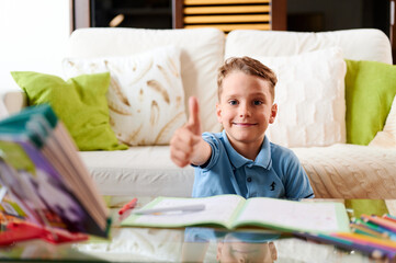 Caucasian school boy doing homework and shows thumb up gesture