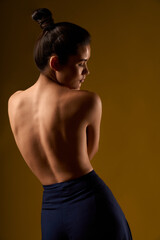 Back view of slim girl with hair bun standing, bending, looking down. Flexible female with bare...