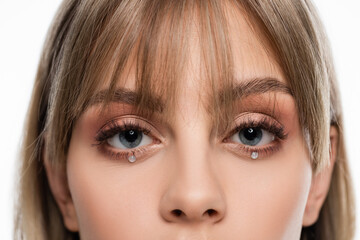 cropped view of young woman with bangs and shiny rhinestones under blue eyes isolated on white