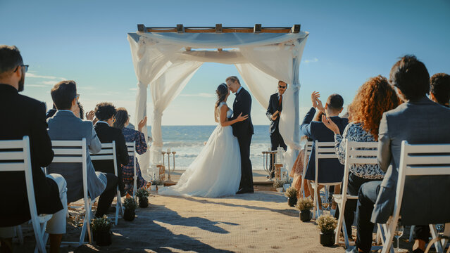 Beautiful Bride and Groom During an Outdoors Wedding Ceremony on a Beach Near the Ocean. Perfect Venue for Romantic Couple to Get Married, Kiss and for Friends with Multiethnic Cultures to Celebrate.