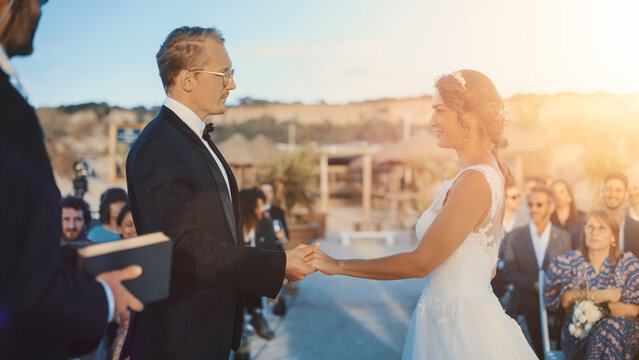 Beautiful Bride and Groom During an Outdoors Wedding Ceremony on an Ocean Beach at Sunset. Perfect Venue for a Couple to Marry, Exchange Rings, Kiss and Share Celebrations with Multiethnic Friends.
