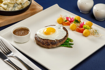 Beef egg meat on white plate on blue tablecloth in restaurant