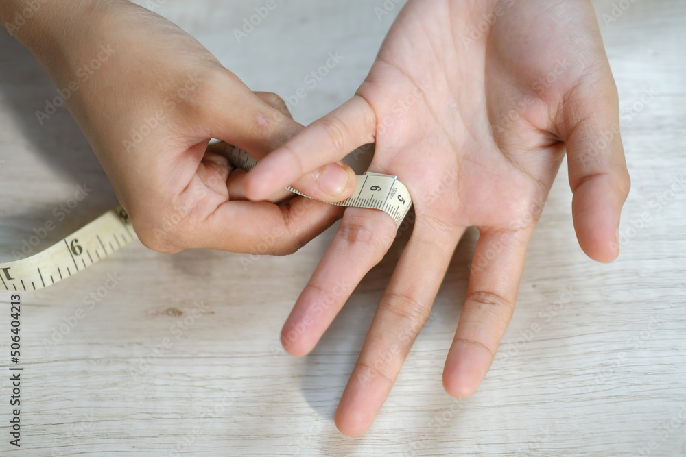 Wall mural closeup of woman's hand measuring finger with measuring tape