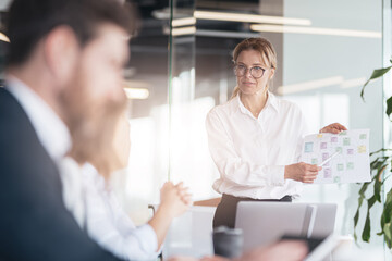 Business mature woman talking on presentation financial statistics at briefing in office.