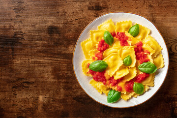 Ravioli with tomato sauce and basil. A plate of stuffed pasta, shot from above, vegetarian dinner on a dark rustic wooden background with copy space