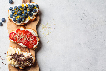 Fruity vegetarian toasts for breakfast on gray background. Bread slices with ricotta, berries,...