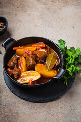 Beef stew with potatoes, carrots in tomato sauce in black pot,  dark background.