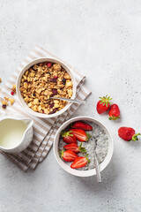 Homemade granola bowl and chia pudding with strawberries, gray background, top view.