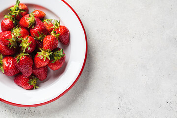 Fresh organic strawberries in white plate, top view, gray background.