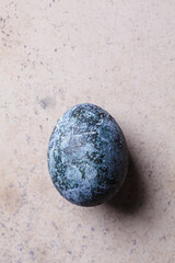 Single Easter egg painted in trendy denim blue, brown background.