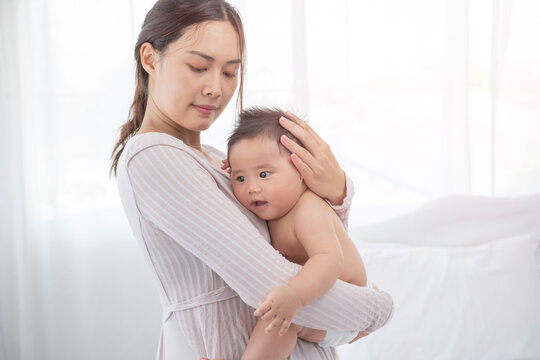 happy loving family. asian mother lifting and playing with baby in the bedroom, asia mother hug cuddle little infant or toddler, enjoy tender family moment, motherhood, childcare concept.