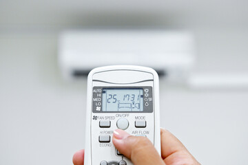 Closeup hand adjust temperature of air conditioner at 25 degree C via remote control. Save energy concept