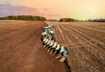 Tractor with plow on field cultivating. Green tractor plowing field on sunset. Cultivated land and...