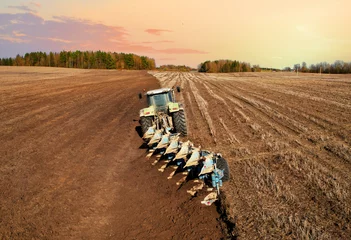 Foto op Aluminium Tractor with plow on field cultivating. Green tractor plowing field on sunset. Cultivated land and soil tillage. Agricultural tractor on field cultivation. Tractor disk harrow on plowing, aerial view. © MaxSafaniuk