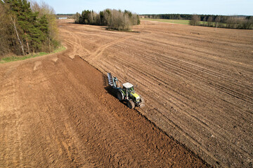 Tractor with plow on soil cultivating. Green tractor plowing field, drone view. Cultivated land and...
