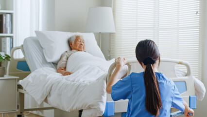 Young Asian woman, nurse, caregiver, carer of nursing home adjusting bed for a senior Asian woman at home.