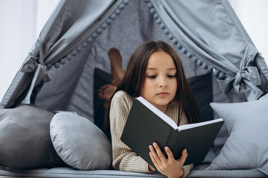 Little girl reading book lying in vigvam