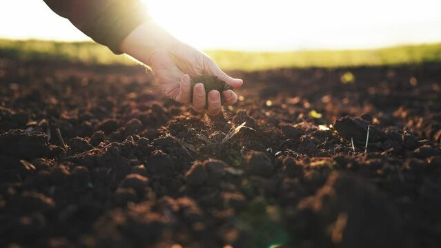 Farmer hand scooping dirt on a field at sunset. Man grabbing the soil dirt from the ground. Close up of male hands touching dry ground in an agricultural field. Concept of agribusiness.
