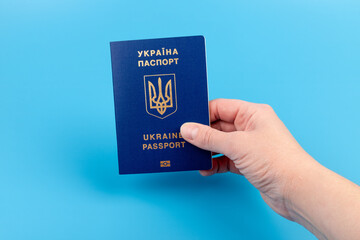 Passport of a citizen of Ukraine in a female hand on a blue background, close-up. Inscription in Ukrainian Ukraine Passport