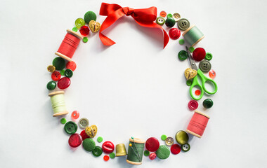 Wreath made of buttons, threads, pins, scissors, thimble red, green and gold color. White background. Copy space