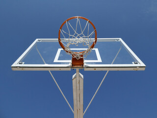 Basketball hoop with net on an outdoor court with sky background, view from below