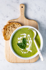 Basil green soup with rustic bread toast on wooden board and white marble background