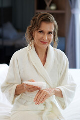 Portrait of happy middle-aged woman applying nourishing hand cream