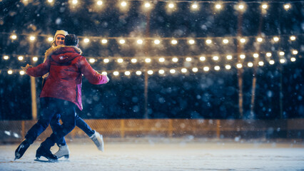 Romantic Winter Snowy Evening: Ice Skating Couple Having Fun on Ice Rink, Spin and Dance. Pair Skating Outdoors. Portrait of Young People, Boyfriend and Girlfriend in Love, Smile, Magical Wintertime - obrazy, fototapety, plakaty