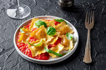 Ravioli with tomato sauce and fresh basil leaves on a plate, Italian pasta dish, on a dark background with a glass of white wine