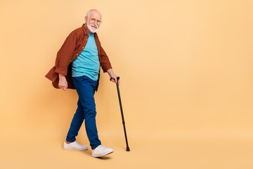Full body photo of good mood pensioner man go on walk take care of his health isolated on beige...