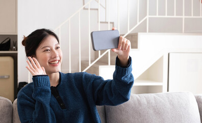 Portrait beautiful young asian woman use smart mobile phone on sofa in living room interior - obrazy, fototapety, plakaty