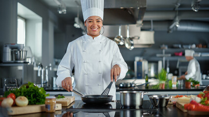 Restaurant Kitchen: Portrait of Black Female Chef in Action, Uses Pan to Cook Delicious, Traditional Authentic Food, Looks at Camera and Smiles. Healthy gourmet Dishes. Medium Wide Shot