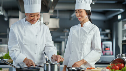 Restaurant Kitchen: Asian and Black Female Chefs Preparing Dish, Tasting Food and Doing High-Five in Successful Celebration. Two Professionals Cooking Delicious, Authentic Food, Healthy Meals Recipe