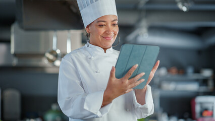 Restaurant Kitchen: Black Female Chef Cooking Delicious and Authentic Food, Uses Digital Tablet...