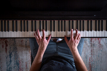 Male hands on the piano keys, top view.