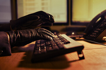 Man attacker hacker in black gloves on his hands working on a computer keyboard at an office desk, close-up