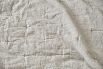 Beige crumpled bed linen fabric texture. Background of white cotton bedspread