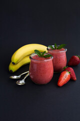 Smoothie with strawberry and banana in the glass jar on the black background. Copy space. Location vertical.