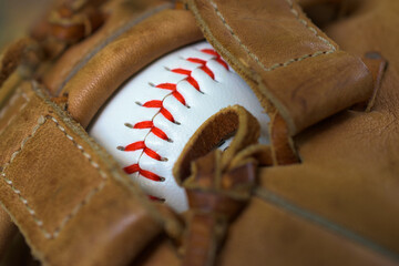 White Baseball with Red Stitching.  Baseball shows through the rawhide webbing of a baseball glove.