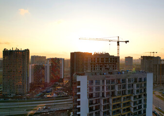 Crane during the construction of a residential building at sunset. Construction site at sunset with a tower crane and unfinished buildings and residential houses skyscrapers.