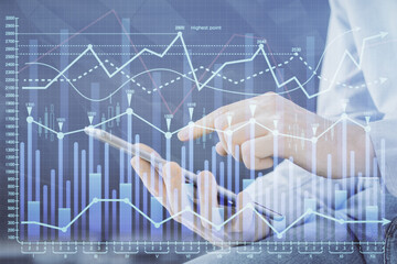 Double exposure of man's hands holding and using a digital device and forex graph drawing. Financial market concept.