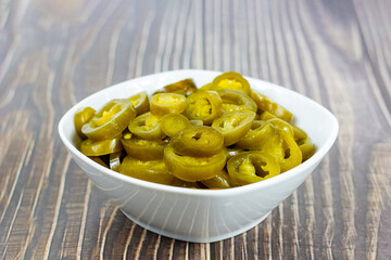 Green spicy sliced marinated jalapeno pepper in white bowl on light background in the kitchen.