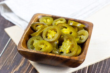 Green spicy sliced marinated jalapeno pepper in wooden bowl on light background in the kitchen.