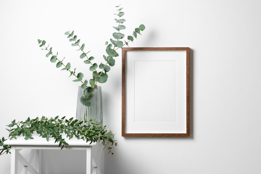 Blank frame mockup for artwork, quote or photo on white wall with natural eucalyptus twigs.