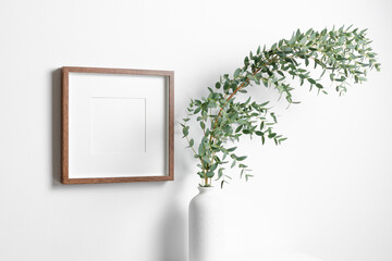 Blank square frame mockup for artwork or print on white wall with eucalyptus plant in vase