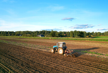 Tactor with disk harrow on plowing field. Cultivated land and soil tillage. Blue Tractor with disc cultivator on land cultivating. Agricultural tractor on soil cultivation field. Plough plowed.