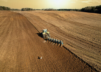 Tractor with plow on field cultivating. Green tractor plowing field on sunset. Cultivated land and...