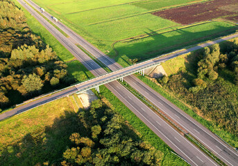 Highway along a green field with a road bridge and traffic interchange, view from the air. Cars and...
