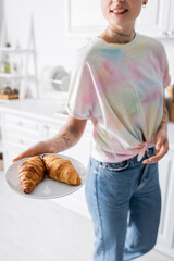 cropped view of smiling woman holding plate with tasty croissants in kitchen